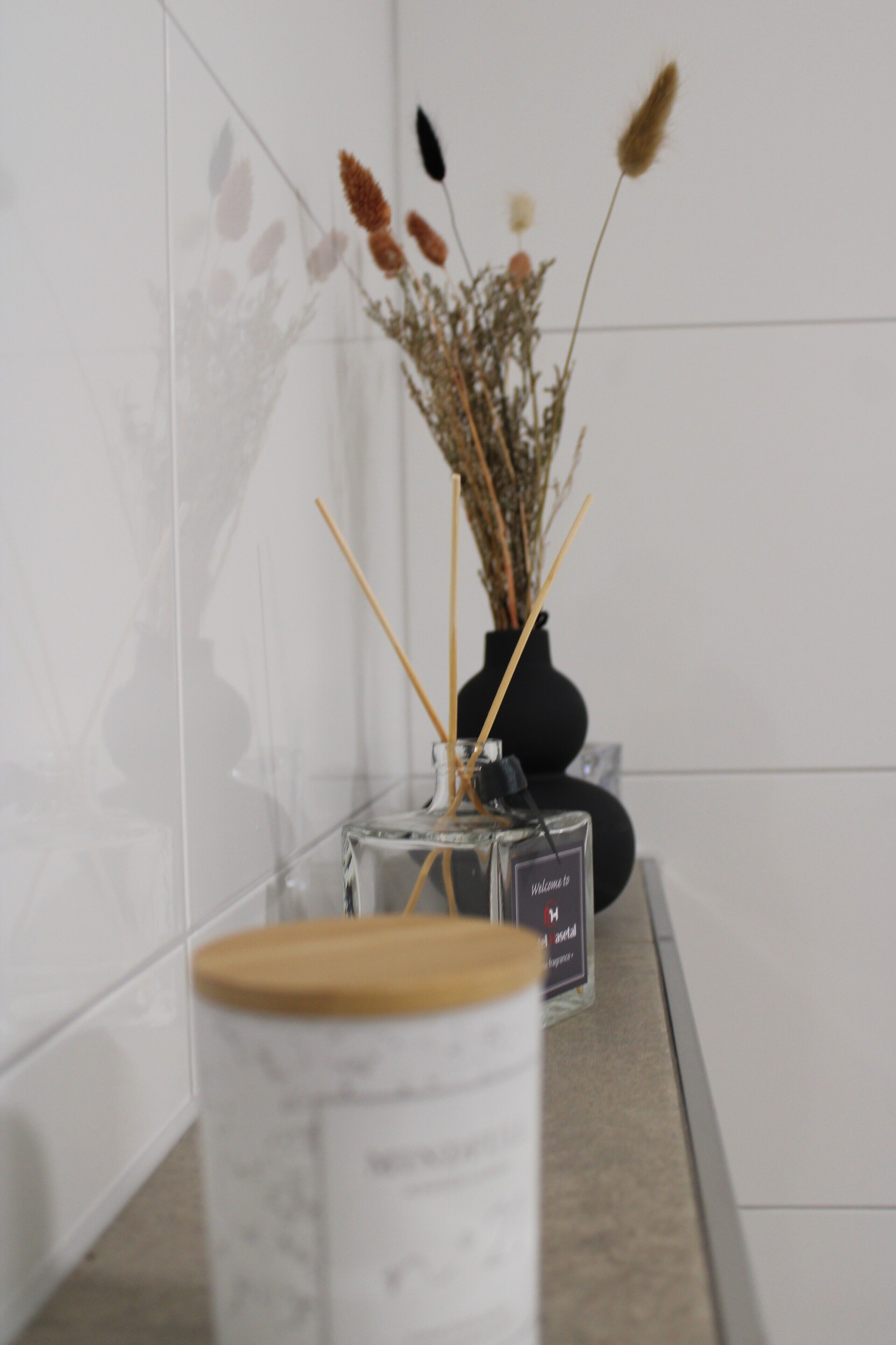 A clear view of a room with a white tiled wall, a black vase with dried flowers, and a small rectangular object on the counter.