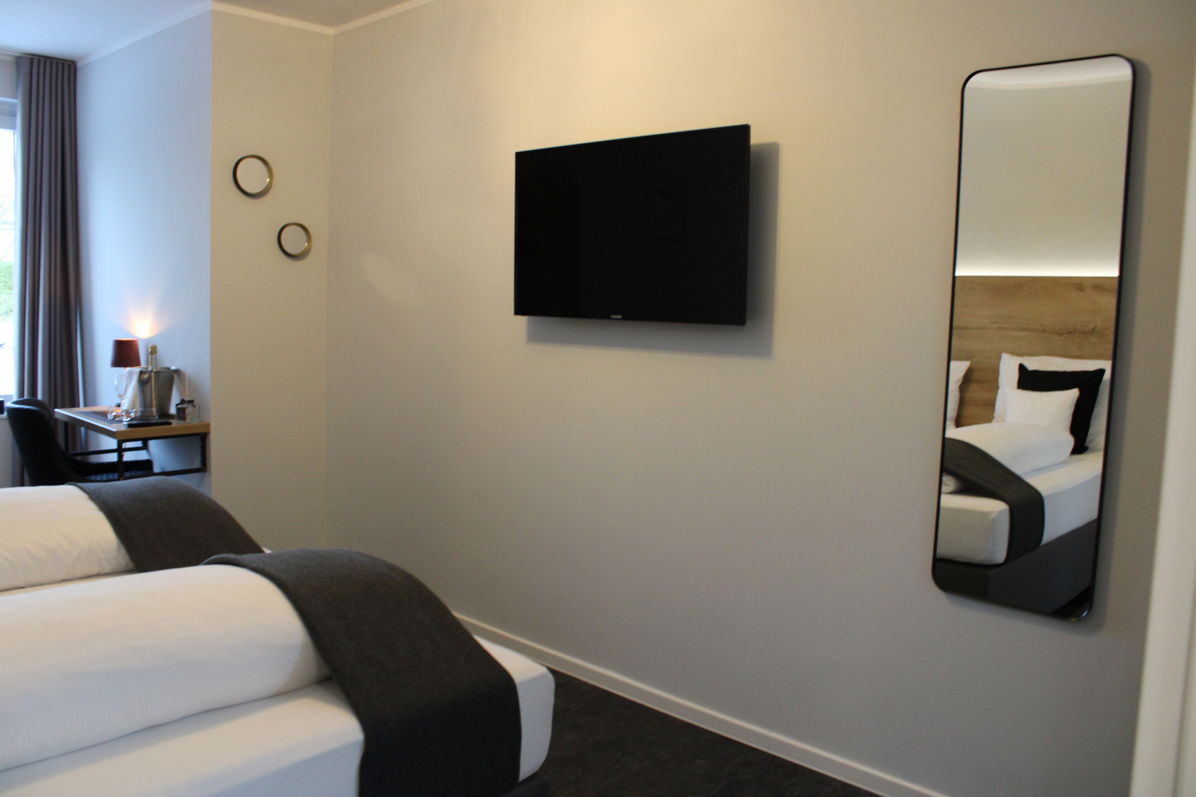 Hotellihuone, jossa on sänky, seinälle asennettu televisio, yöpöytä lampun kanssa ja peili, joka heijastaa sängyn.