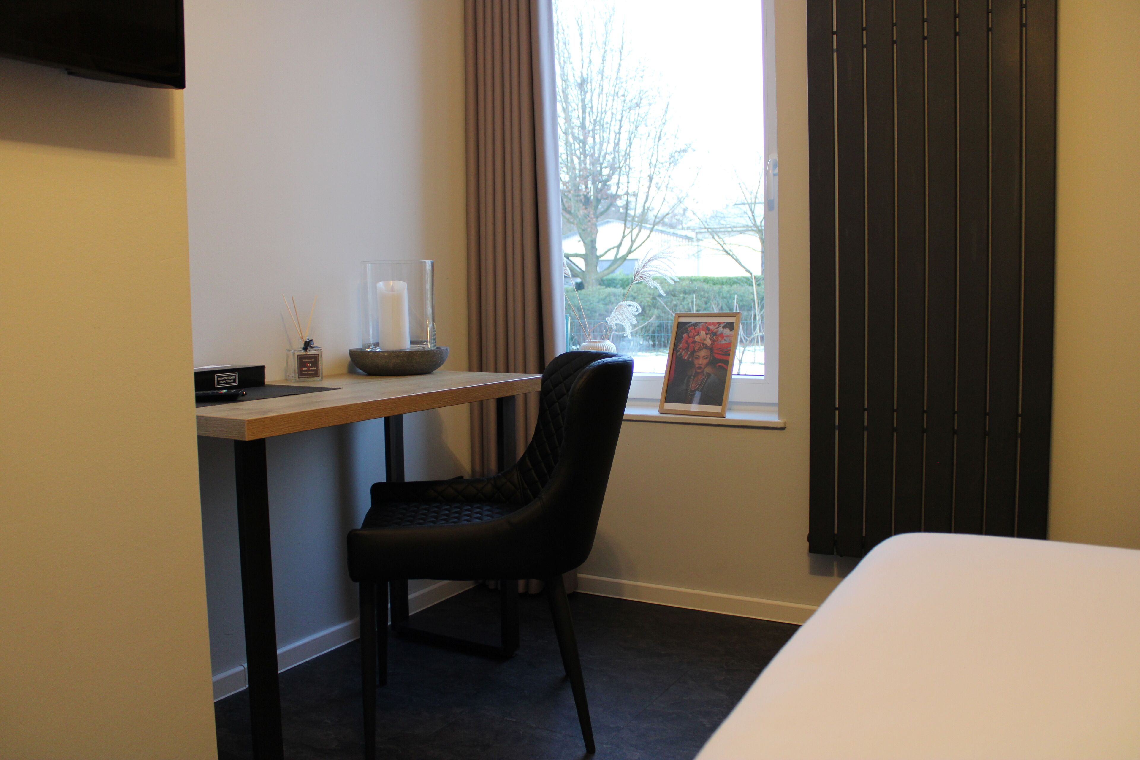 A hotel room with a bed, a desk with a chair, a window with curtains, and a view of the outside.