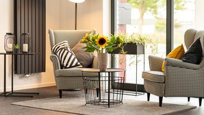 A modern living room with two houndstooth armchairs, a round coffee table, a floor lamp, and a vase with sunflowers.
