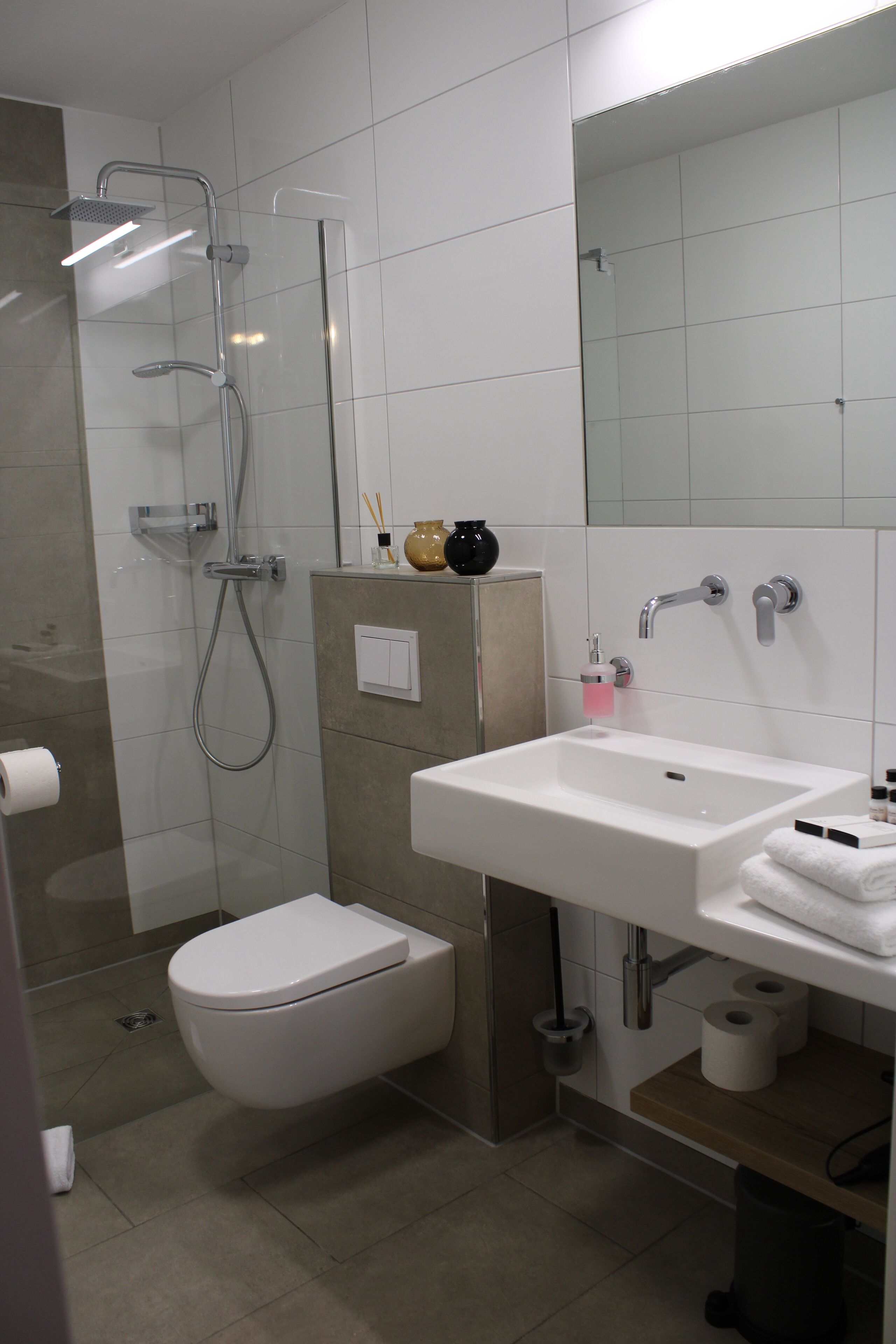 A modern bathroom with a glass shower enclosure, a white toilet, a sink with a mirror, and a towel rack.