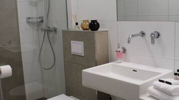 A modern bathroom with a glass shower enclosure, a white toilet, a sink with a mirror, and a towel rack.