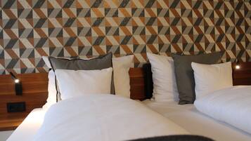 Une chambre d’hôtel avec un mur orné d’un motif géométrique, une tête de lit en bois et un lit bien fait, recouvert de draps blancs et agrémenté de plusieurs oreillers.