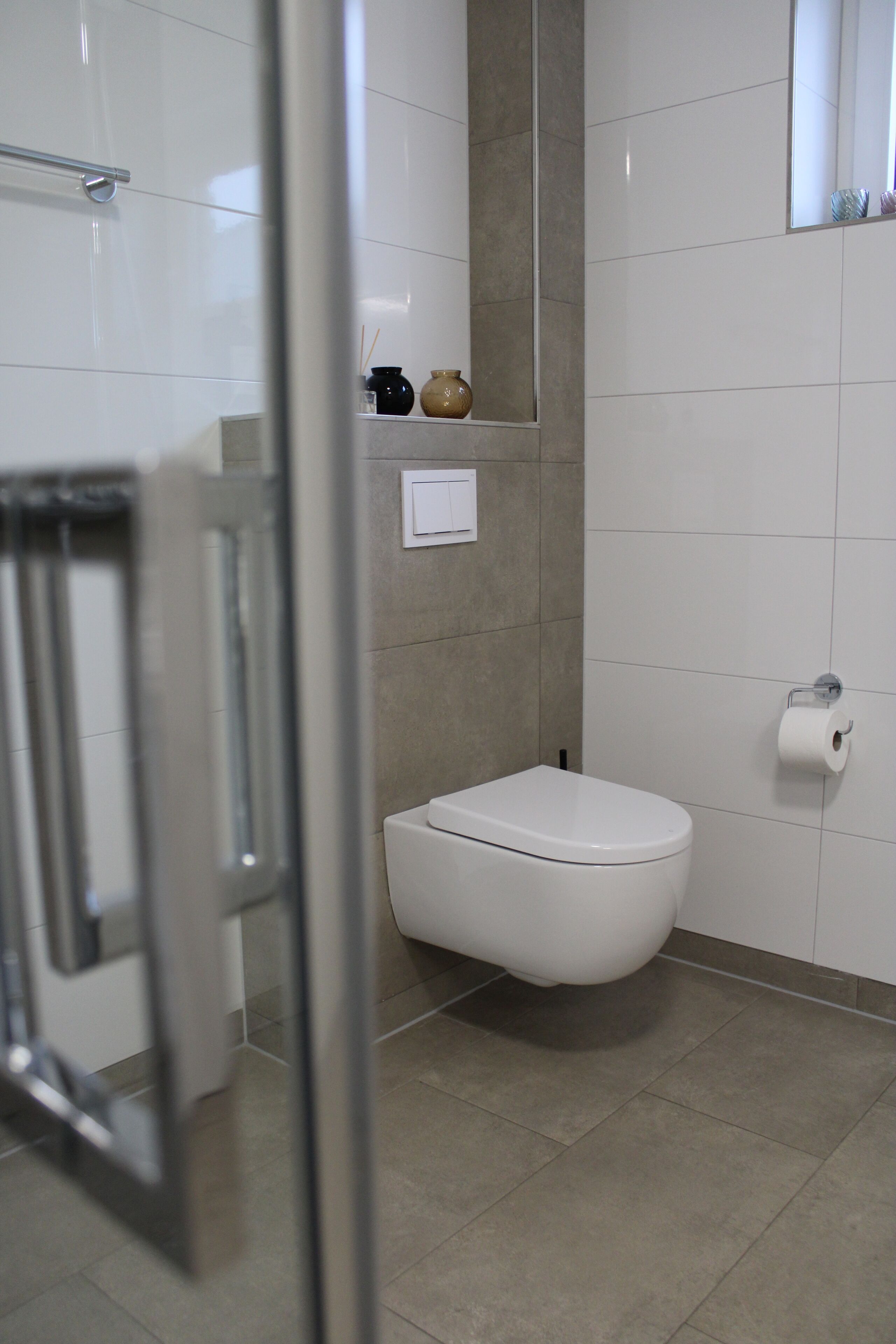 A modern bathroom with a white toilet, a glass shower enclosure, and a small shelf with toiletries.