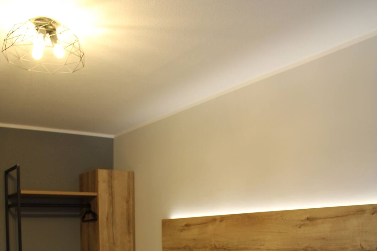 Ein Doppelbett mit Holzüberbau, ein Nachttisch und eine hängende Deckenleuchte.