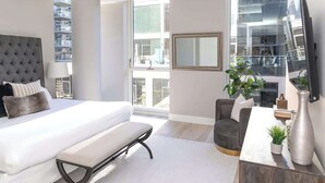 A modern bedroom with a large bed, a bench, a desk with a plant, and a TV. - Luxury Loft Collection COMBO 02/03 | Terrace (Chicago)