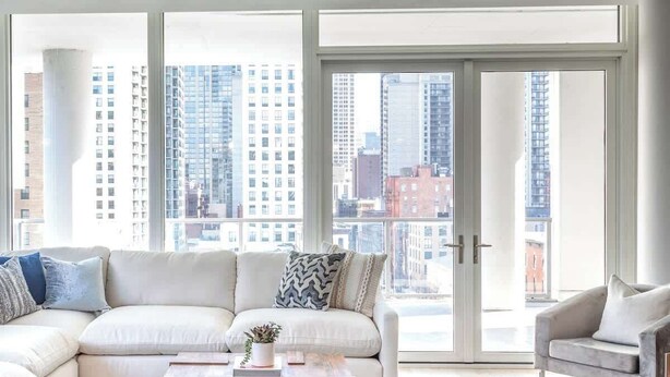 A modern living room with a sectional sofa, a coffee table, and a view of a cityscape through large windows. - Luxury Loft Collection COMBO 02/03 | Terrace (Chicago)