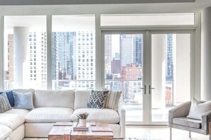 A modern living room with a sectional sofa, a coffee table, and a view of a cityscape through large windows. - Luxury Loft Collection COMBO 02/03 | Terrace (Chicago)