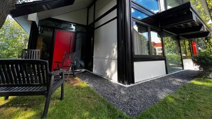 Un edificio moderno con ventanas amplias, una puerta roja y una banca en el exterior.