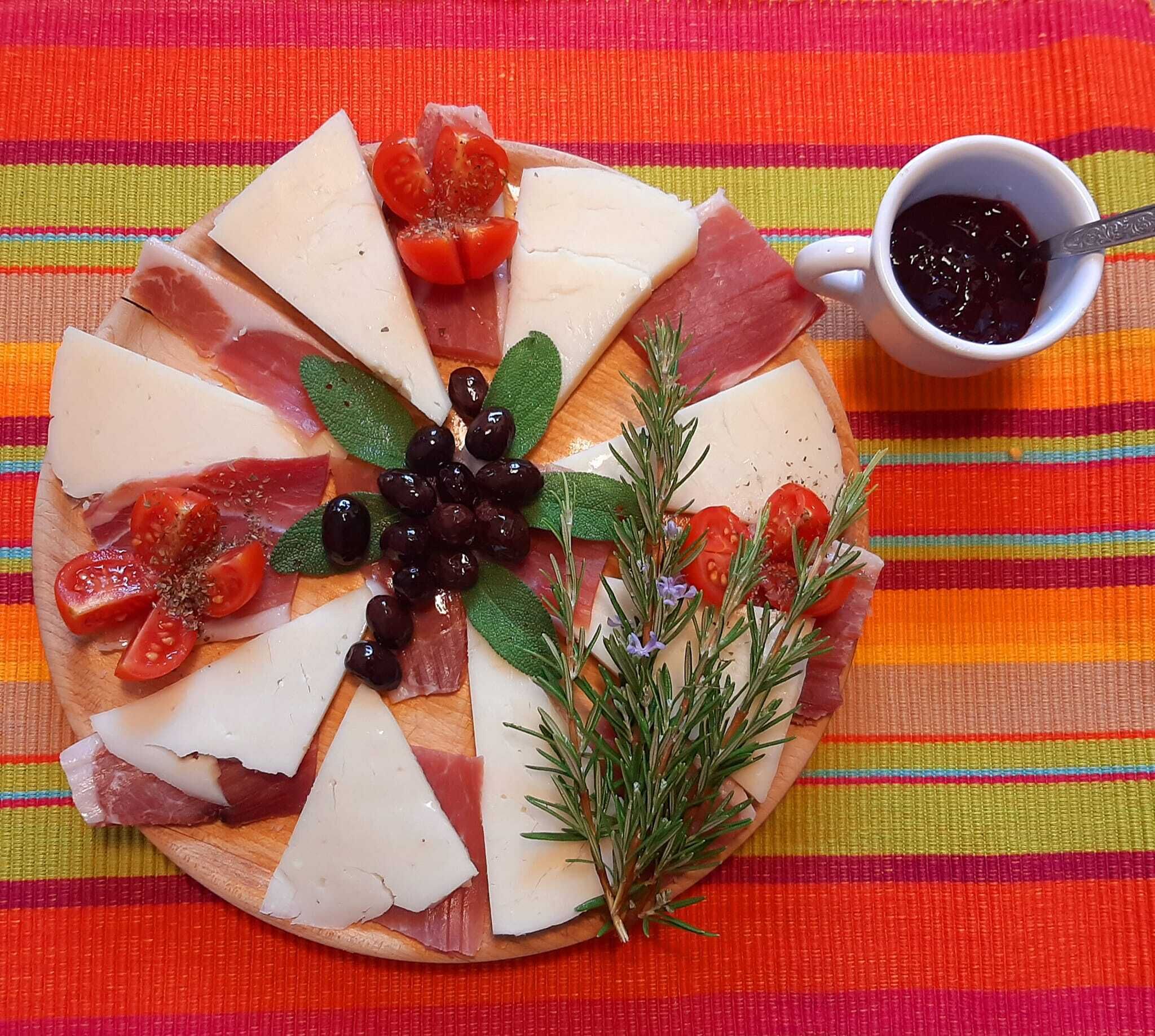 Een charcuteriebord met verschillende vleessoorten, kazen en olijven op een kleurrijke geribbelde tafelkleed.