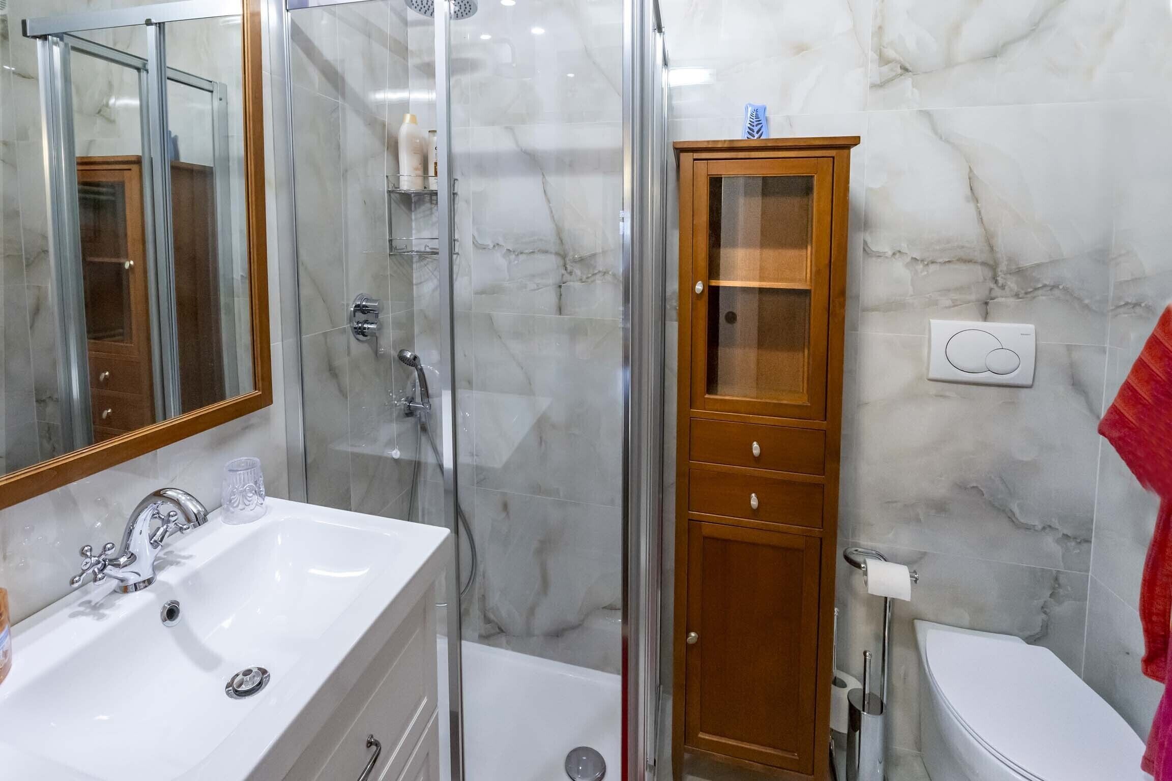 A bathroom with a glass-enclosed shower, a white sink, a wooden cabinet, and a toilet.