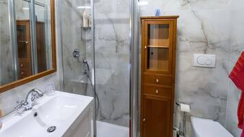 A bathroom with a glass-enclosed shower, a white sink, a wooden cabinet, and a toilet.