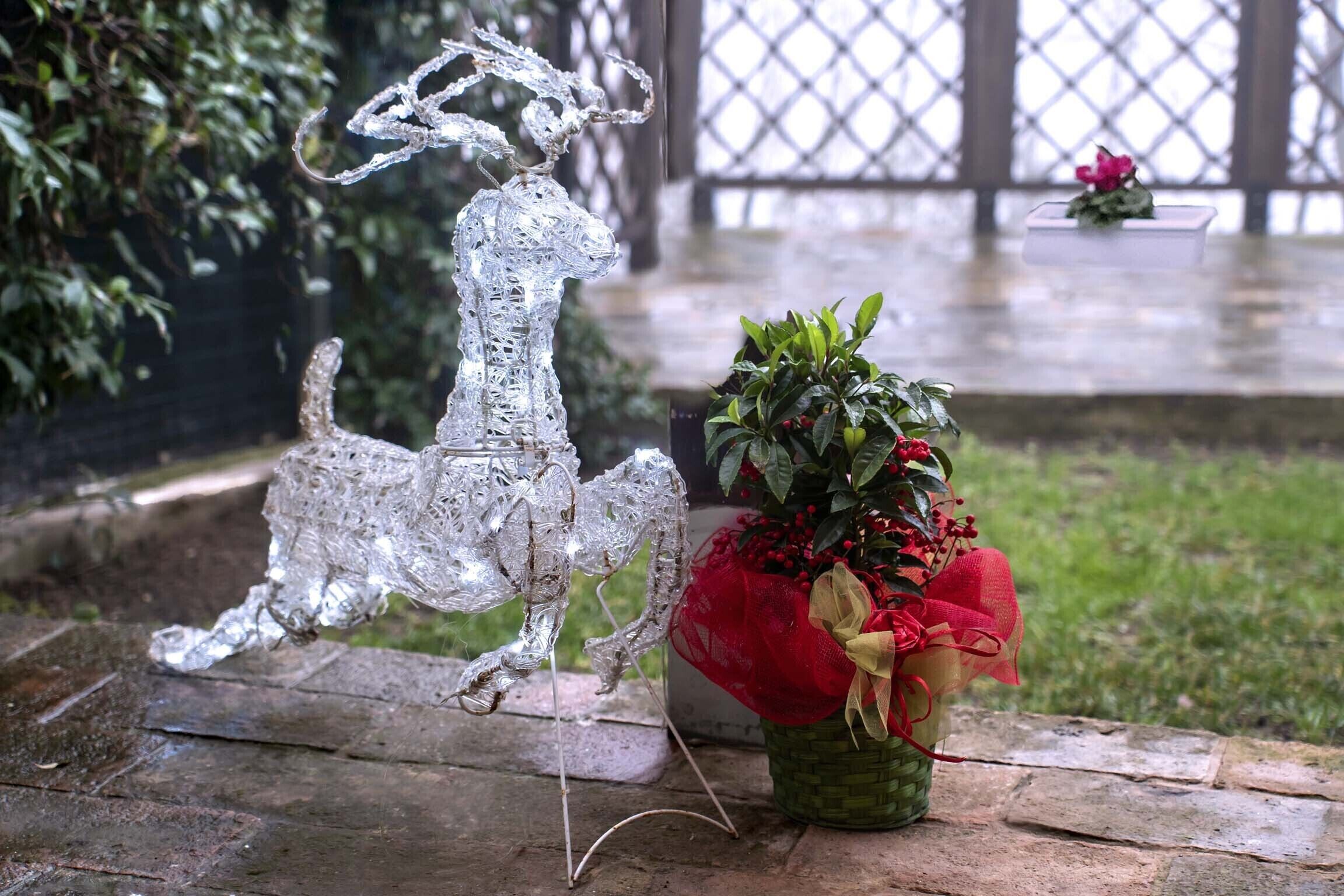 Une sculpture décorative représentant un renne en argent et une plante en pot aux fleurs rouges et jaunes, le tout posé sur une surface en pierre.
