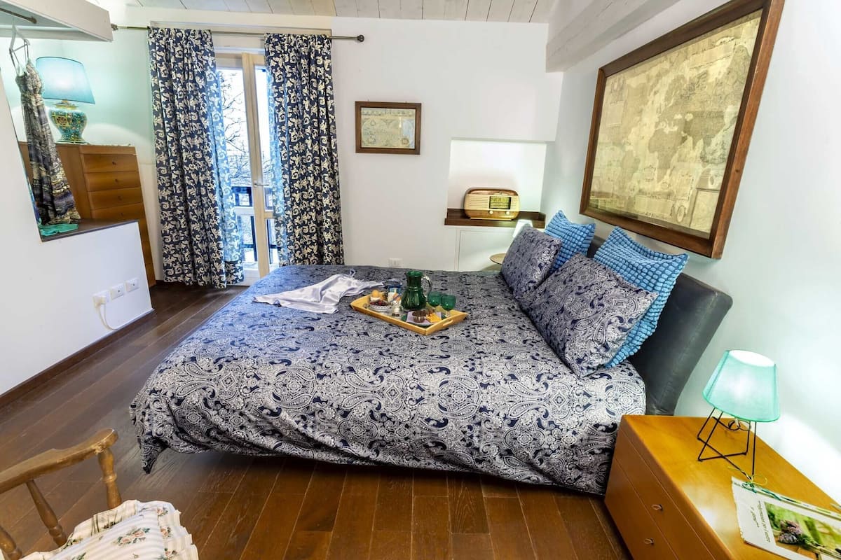 A bedroom with a bed, a dresser, a chair, a lamp, a map on the wall, and a window with curtains.