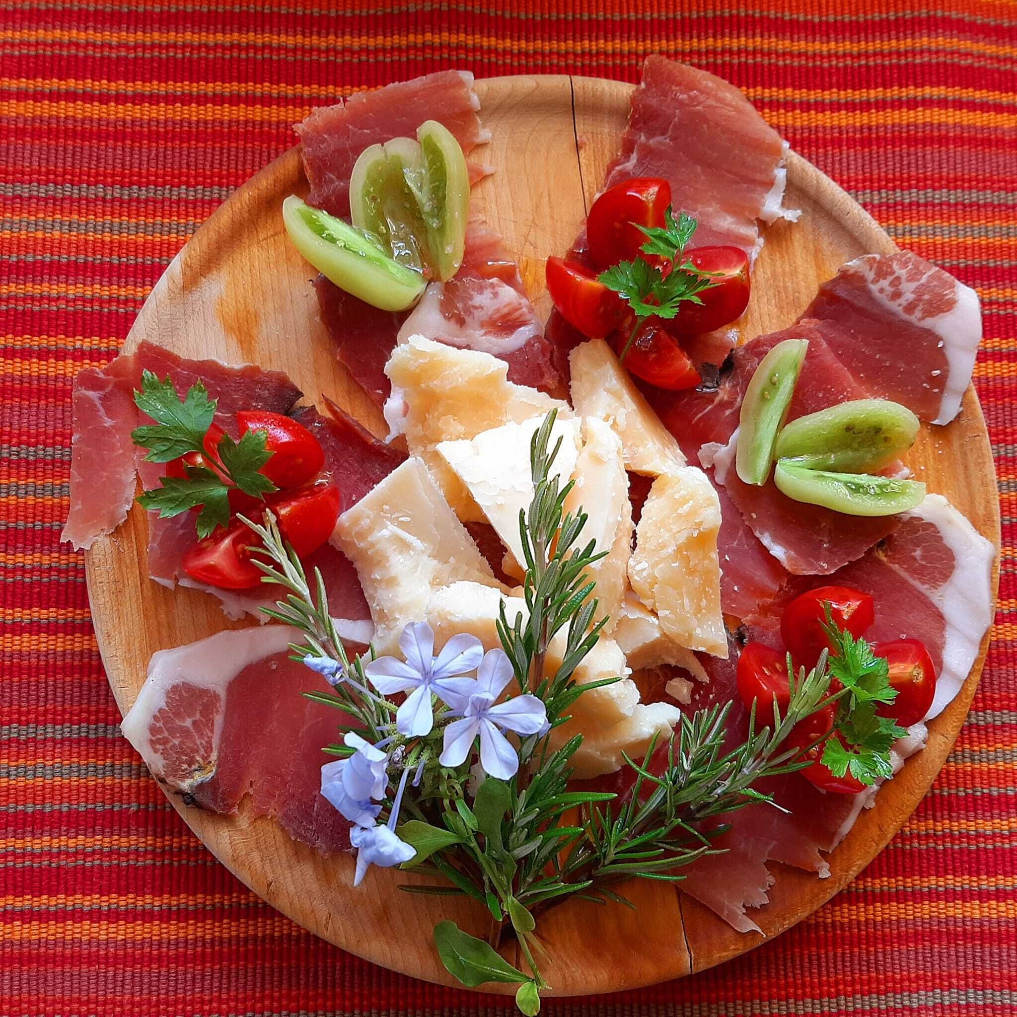 A wooden board with various meats, cheese, and vegetables.