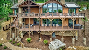 Una cabaña de madera de varios pisos, con base de piedra, ventanas amplias y zonas de estar al aire libre.