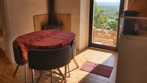 Una habitación con una mesa, sillas, chimenea, vistas a través de una puerta y una pequeña zona de cocina.