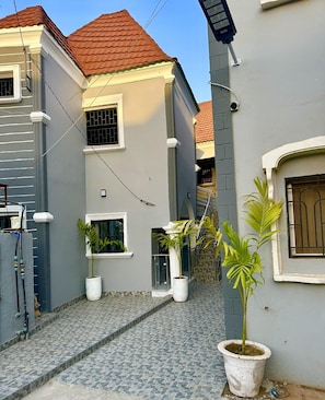A residential building with a tiled courtyard, potted plants, and a red-tiled roof. - Sun Rise Apt #5 The Retreat Apartments (Brusubi)