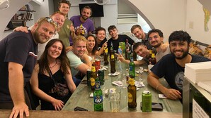 Un groupe de personnes s’est réuni autour d’une table où étaient disposées différentes bouteilles et différents verres, dans une pièce dont un mur était en briques et où un téléviseur était fixé au mur.