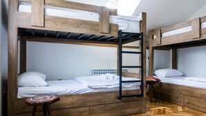 Une chambre avec un lit superposé, une petite échelle en bois, un petit tabouret et un tapis à motifs sur le sol.