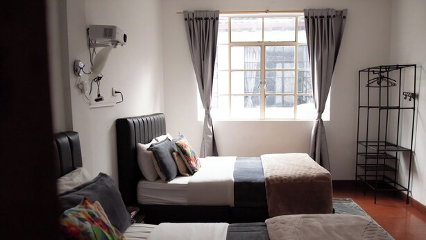 A room with a bed, bedside table, lamp, window with curtains, and a metal rack. - Casa Samor (Bogotá)