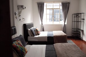 A room with a bed, bedside table, lamp, window with curtains, and a metal rack. - Casa Samor (Bogotá)