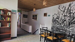 A room with a dining area featuring chairs and a table, a bookshelf with books, a wall with a mural, and a staircase leading to another room. - Casa Samor (Bogotá)