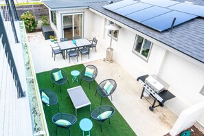 Un jardin avec une terrasse, un barbecue et un coin repas comprenant des chaises et une table.