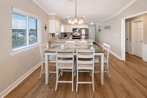 A modern kitchen with white cabinetry, a central island, and a dining area with four chairs. - Oceanfront 2 BR Condo with Shared Pool! Sea Shadow 406  (Surfside Beach)