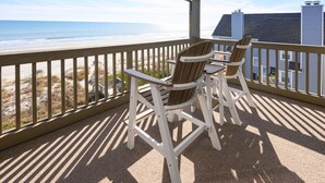 A covered outdoor area with two Adirondack chairs and a table, overlooking a beach with a fence and buildings in the background. - Oceanfront 2 BR Condo with Shared Pool! Sea Shadow 406  (Surfside Beach)