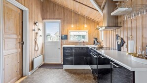 A modern kitchen with wooden walls, a stone-tiled floor, and a view through a window.