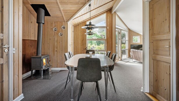 A cozy room with a wooden interior, a round table with chairs, a fireplace, and large windows offering a view of the outdoors.