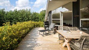 A wooden deck with outdoor furniture, a grill, and a view of a garden and trees.
