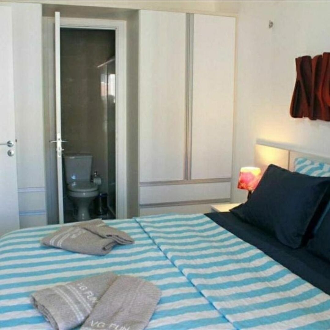 A hotel room with a bed, a nightstand with a lamp, a bathroom with a toilet and shower, and a door.