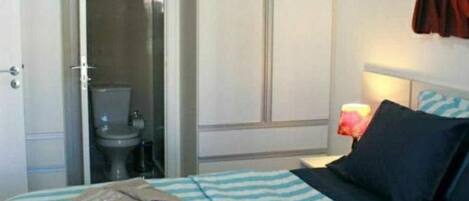 A hotel room with a bed, a nightstand with a lamp, a bathroom with a toilet and shower, and a door.