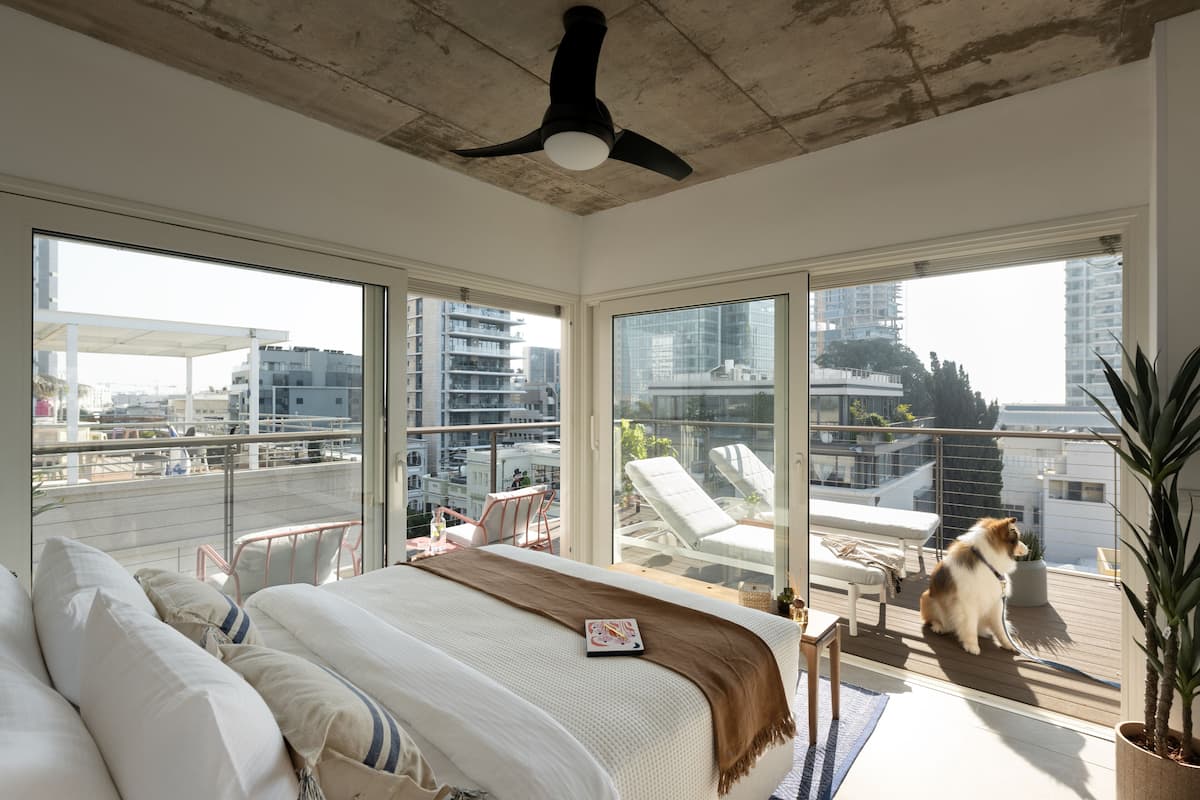 Un dormitorio moderno con una cama grande, un ventilador de techo y un balcón con vista a la ciudad.