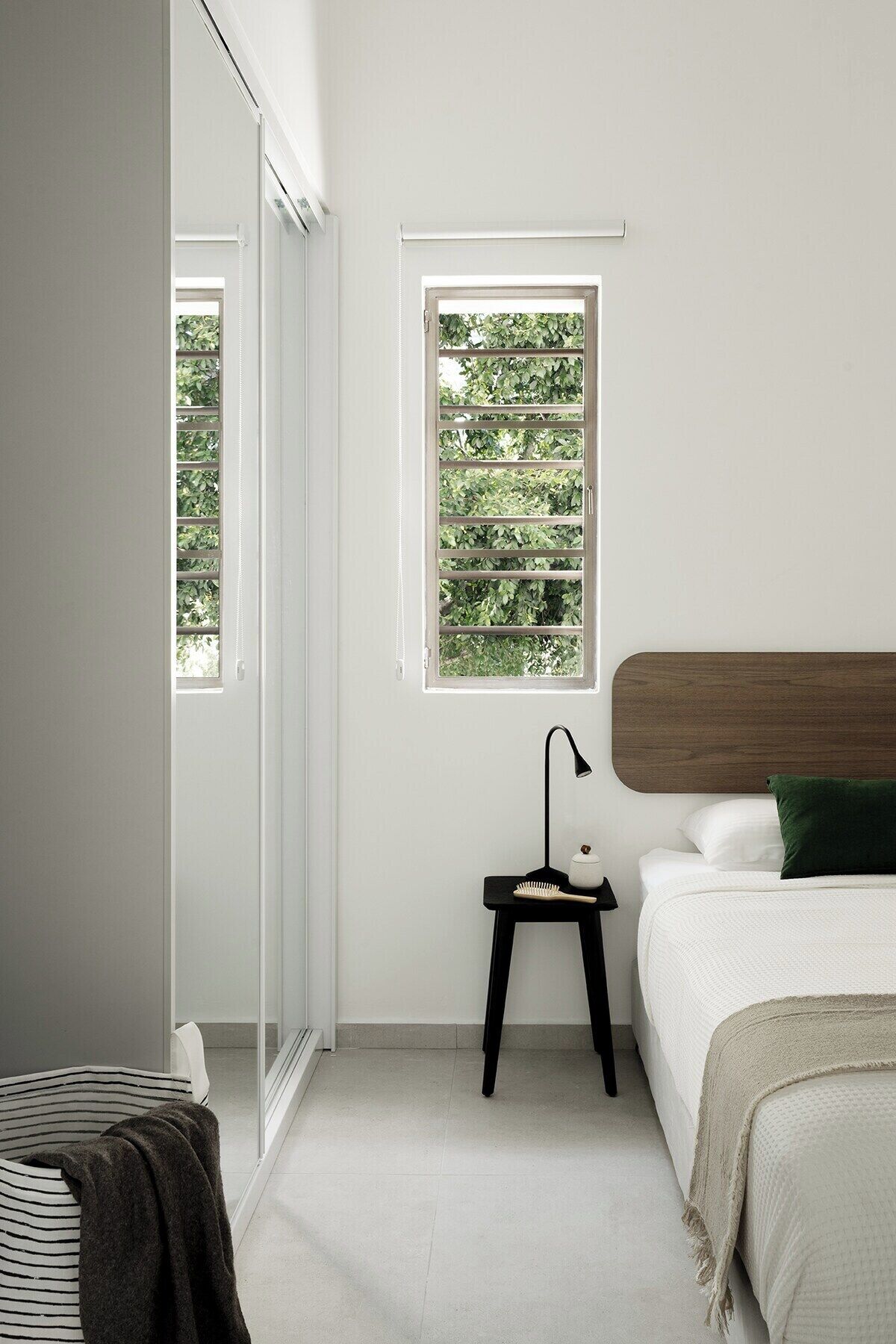 Ein Schlafzimmer mit Bett, Nachttisch mit Lampe, Fenster mit Blick ins Grüne und ein Streifenstuhl.