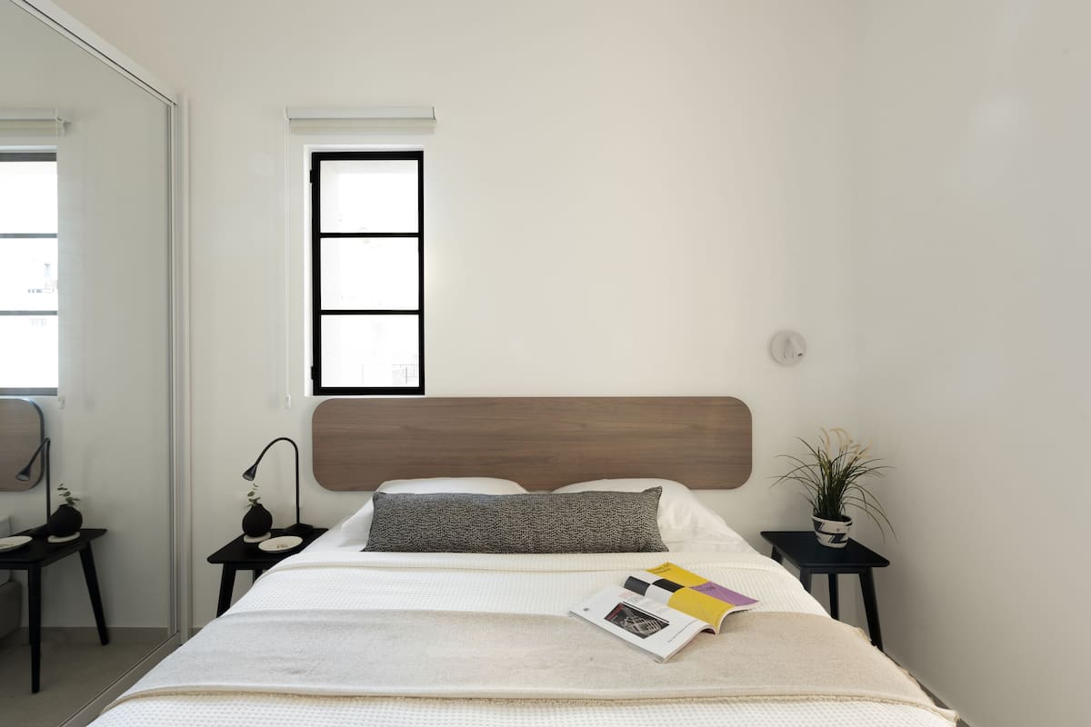 Un dormitorio moderno con una cama grande, un ventanal y dos mesitas de noche con lámparas y objetos decorativos.