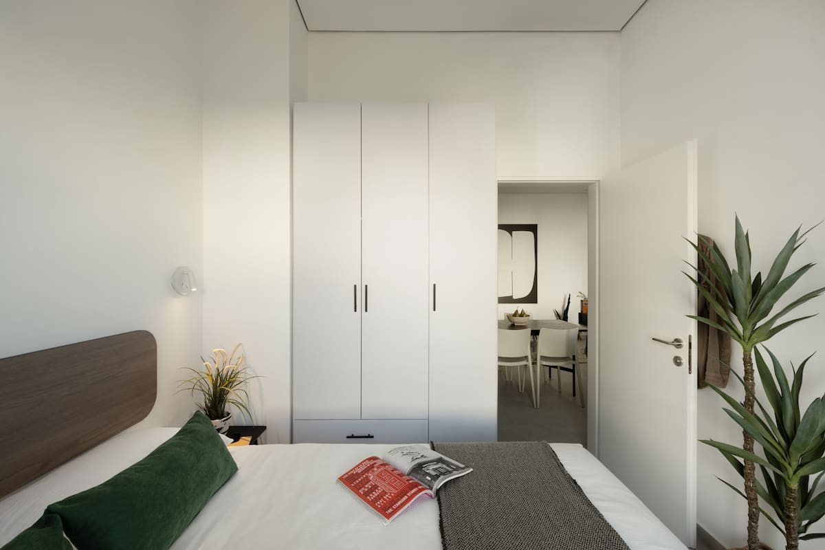 Un dormitorio moderno con una cama, una mesita de noche, un armario y un área de comedor al fondo.
