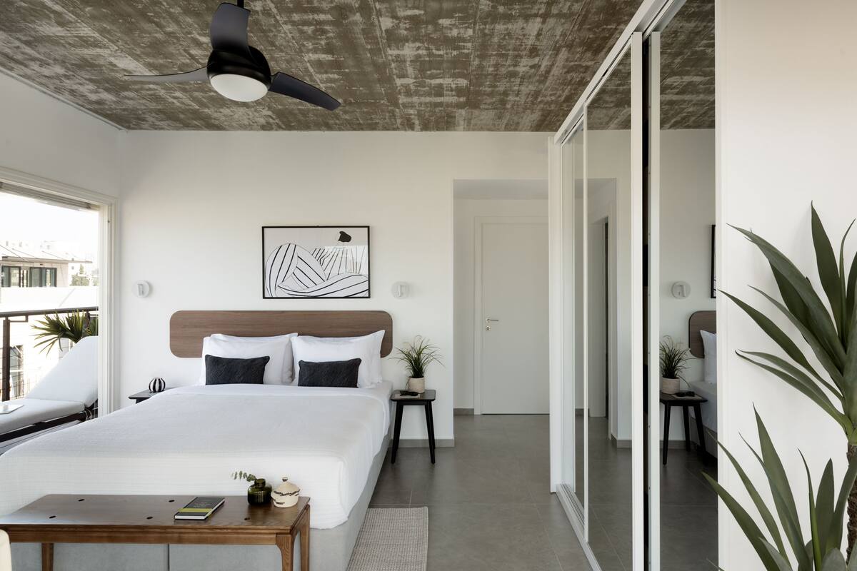 Un dormitorio moderno con una cama grande, ventilador de techo, vistas a la ciudad y un balcón.