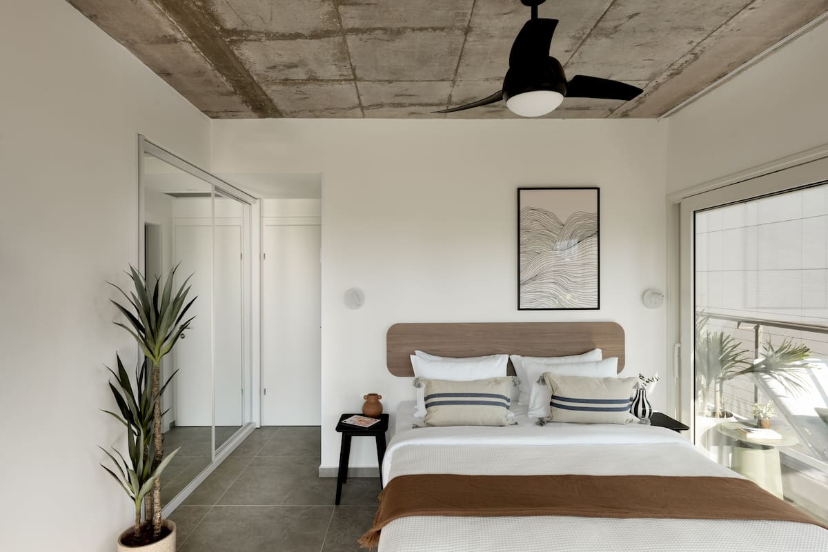Un dormitorio moderno con una cama grande, un ventilador de techo, un ventanal y vistas al exterior.