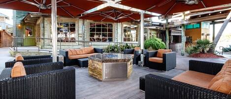 An outdoor seating area with wicker furniture and a glass-top coffee table, under a large red umbrella.