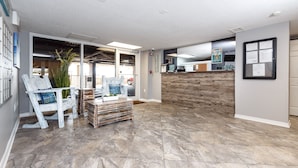 A spacious lobby with a wooden reception desk, a seating area with a white chair, and a large window providing natural light. - GD 410: Shimmering Sea - Sandy Toes, Cozy Condo, The Perfect Pairing! (Fort Walton Beach)