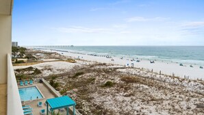 A beach view from a balcony with a pool, beach chairs, and a wooden deck. - GD 410: Shimmering Sea - Sandy Toes, Cozy Condo, The Perfect Pairing! (Fort Walton Beach)