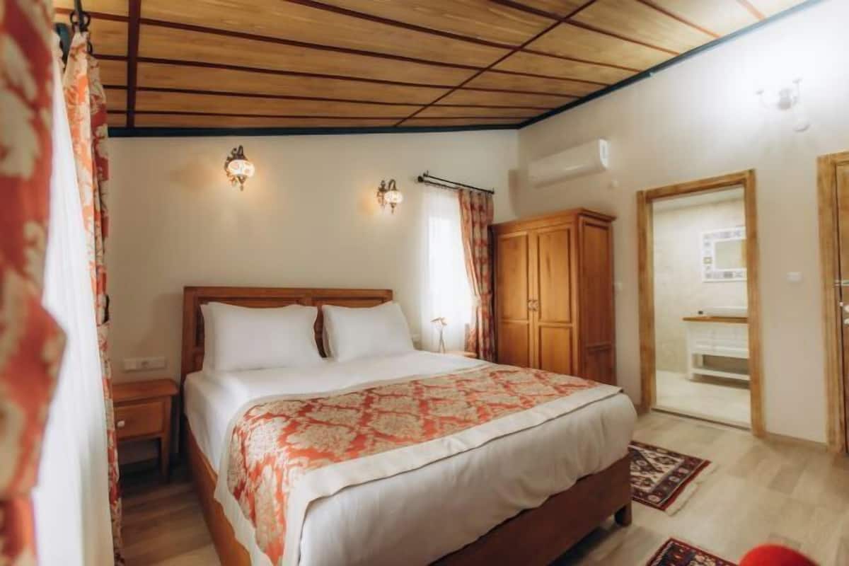 Een slaapkamer met een houten bed, twee bedlampen, een kledingkast en een deur naar een andere kamer.