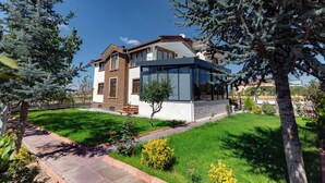 A modern two-story house with a large glass window, a brick exterior, and a well-maintained lawn. - Cappadocia Villa Comfort (Nevsehir)