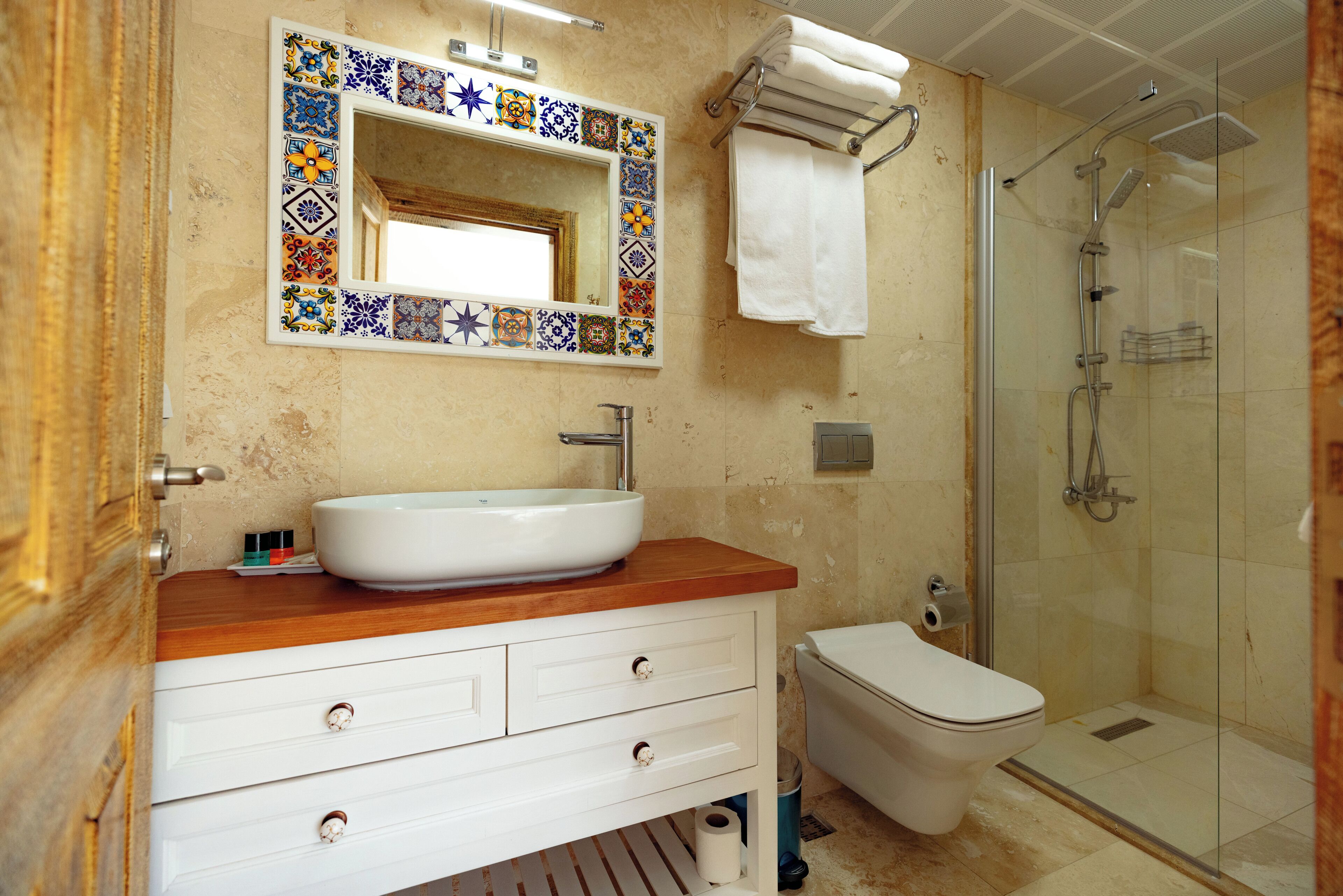 A bathroom with a white sink, a mirror with a colorful tile border, a toilet, and a glass-enclosed shower.