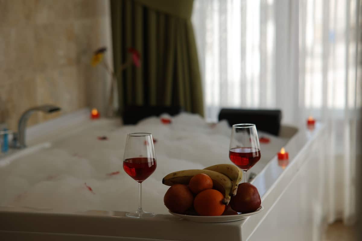 Een badkamer met een bad, twee glazen rode wijn, een fruitschaal en kaarsen.