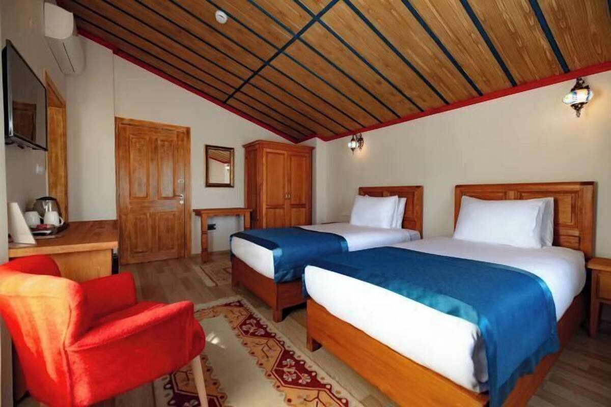 Een kamer met twee bedden, houten meubels, een rode stoel en een plafond met houten balken.
