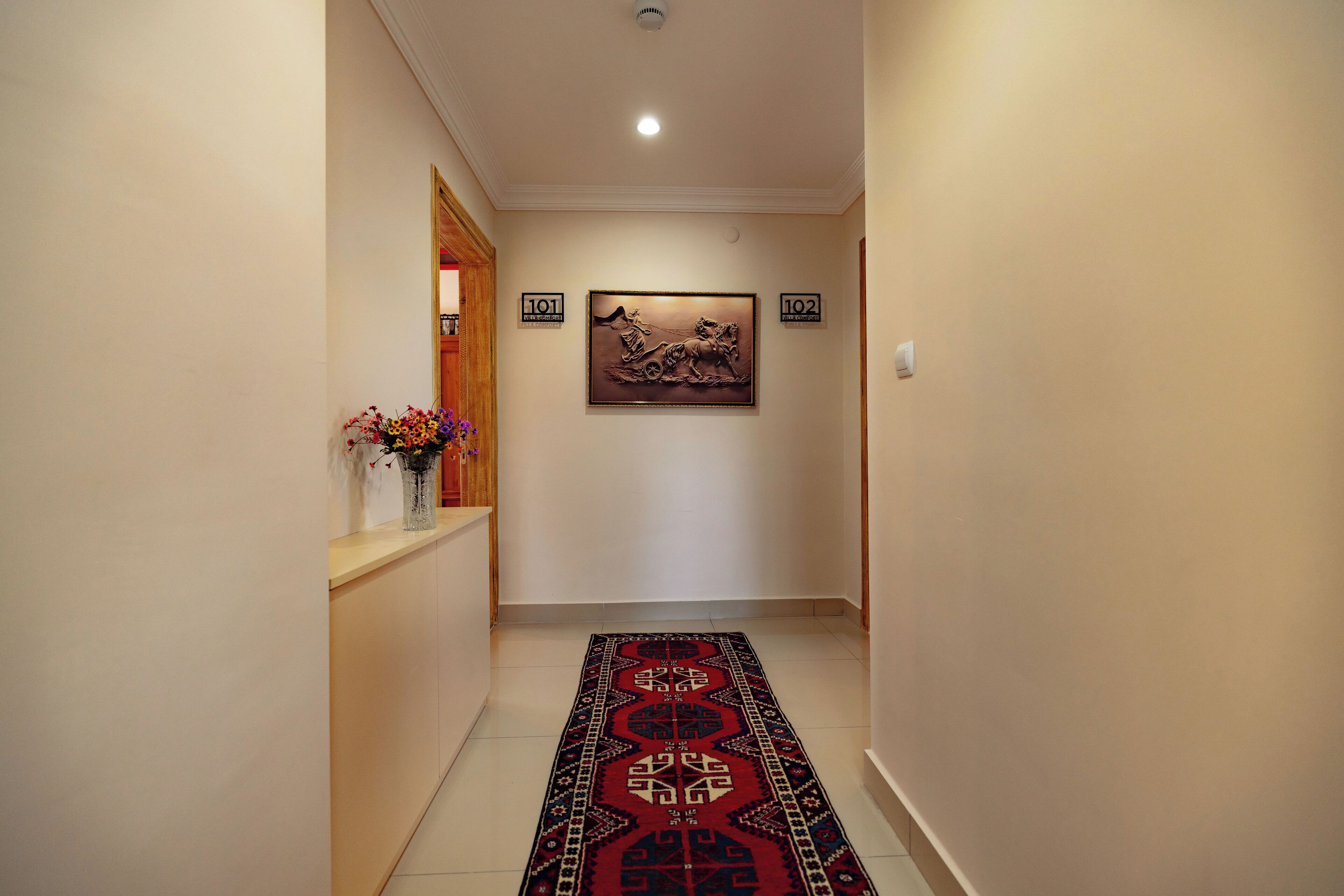 A hallway with a patterned carpet, a vase with flowers, and a framed artwork on the wall.